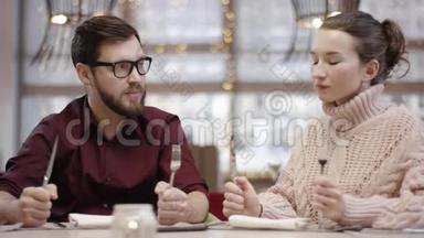 男人和女人静静地坐在桌子旁，等待着拿着刀叉的饭菜